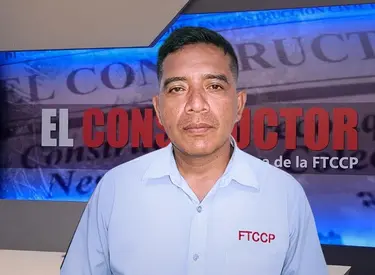 Juan Zela con camisa celeste manga larga frente a un banner del set que dice El Constructor